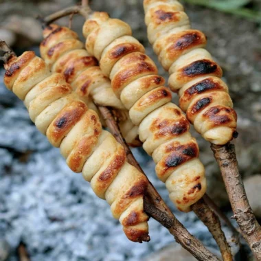 Freshly baked Campfire Bread cooking over a campfire in the woods.