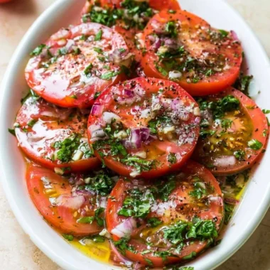 A bowl of vibrant marinated tomatoes garnished with herbs and spices.