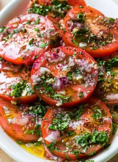 A bowl of vibrant marinated tomatoes garnished with herbs and spices.