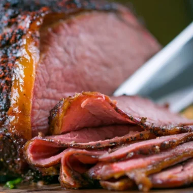 A succulent smoked roast beef on a wooden cutting board, garnished with herbs.