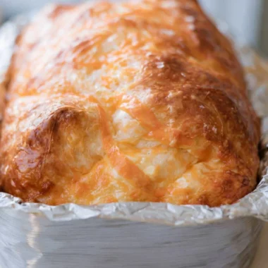 Warm and cheesy sourdough cheese bread loaf on a rustic wooden table