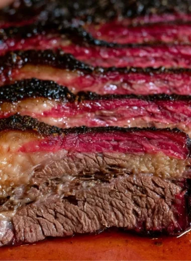 Smoked beef chuck roast served on a wooden cutting board with herbs.