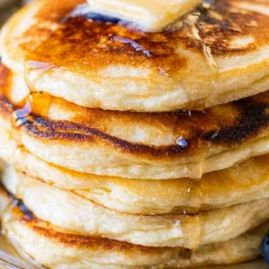 Fluffy and creamy ricotta pancakes stacked on a plate with syrup and berries