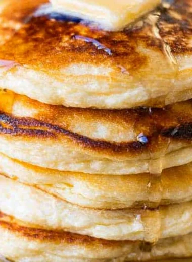 Fluffy and creamy ricotta pancakes stacked on a plate with syrup and berries