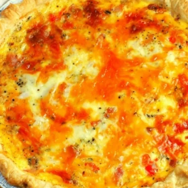 Delicious and easy Bacon Cheese Quiche on a wooden table with fresh herbs.