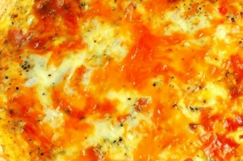 Delicious and easy Bacon Cheese Quiche on a wooden table with fresh herbs.